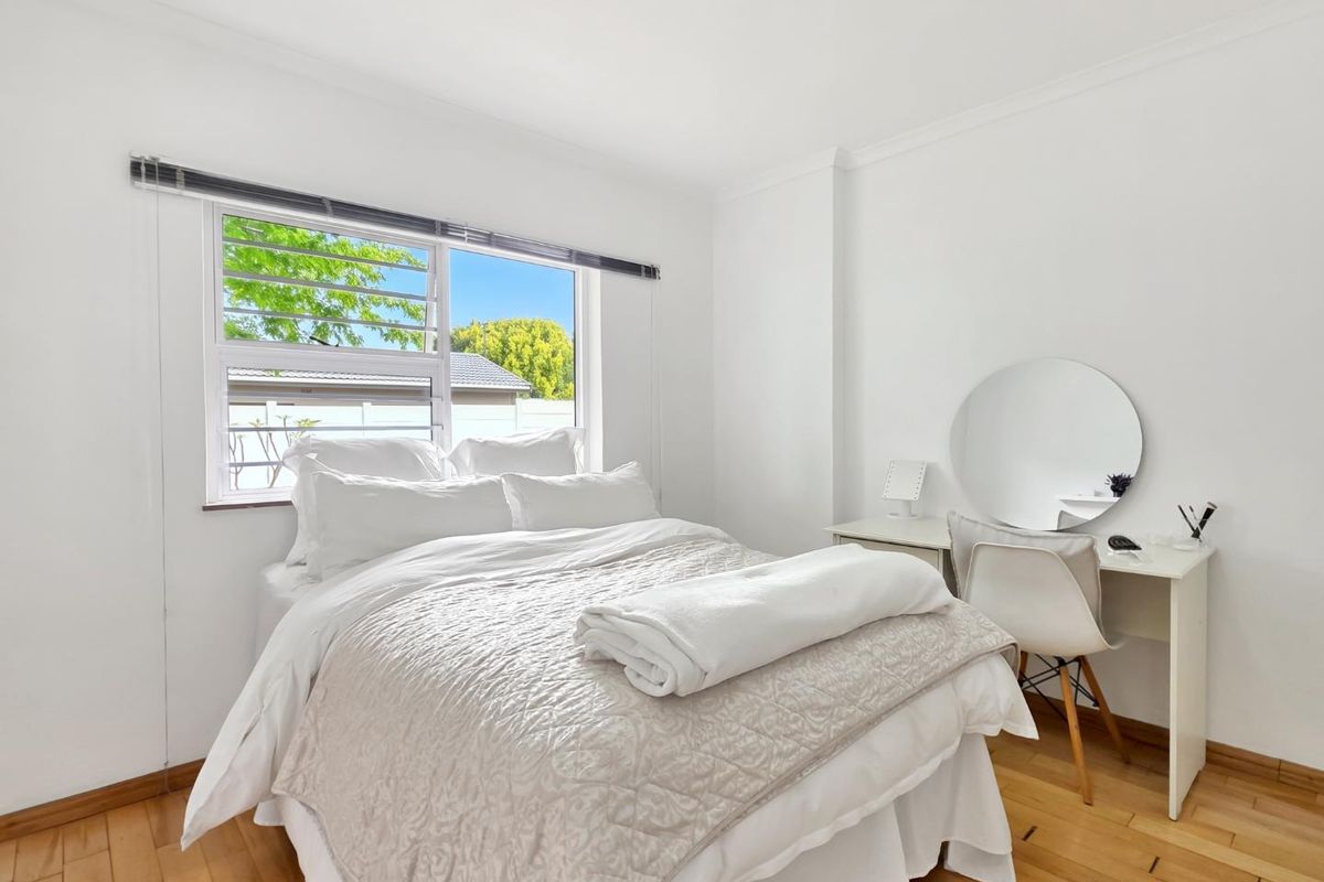 A bright and well-maintained bedroom featuring timber flooring, crisp white walls, and a louver window allowing for natural light and ventilation.