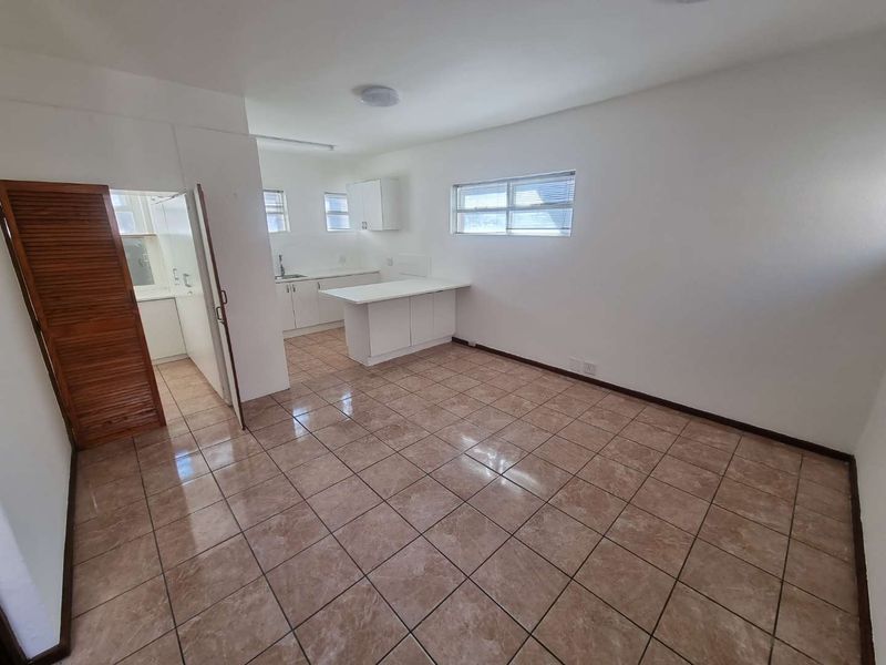 An open-plan living and kitchen area featuring tiled flooring, white cabinetry, and a functional kitchen peninsula in a clean, vacant space.