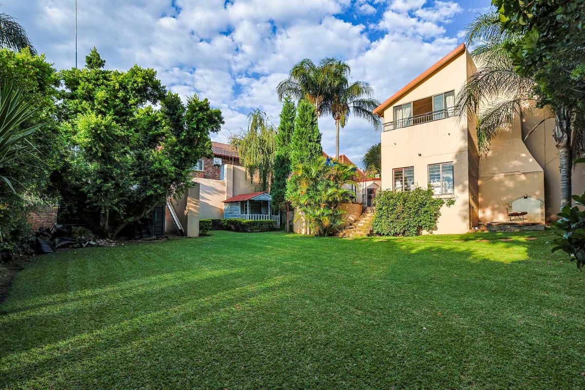A spacious rear garden featuring a well-maintained lawn, mature trees, and a multi-level residential building with a balcony.