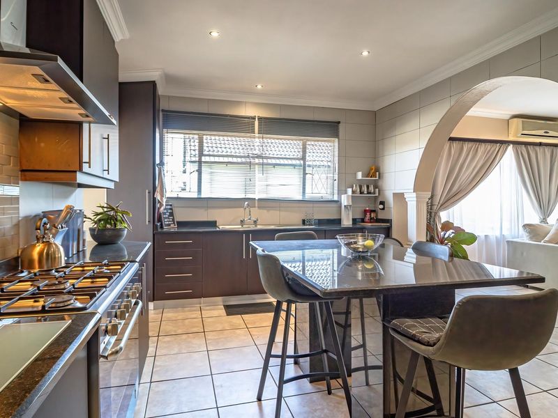Modern kitchen featuring dark cabinetry, granite countertops, gas hob, extractor fan, and tiled flooring, seamlessly connected to the living area via an elegant archway.