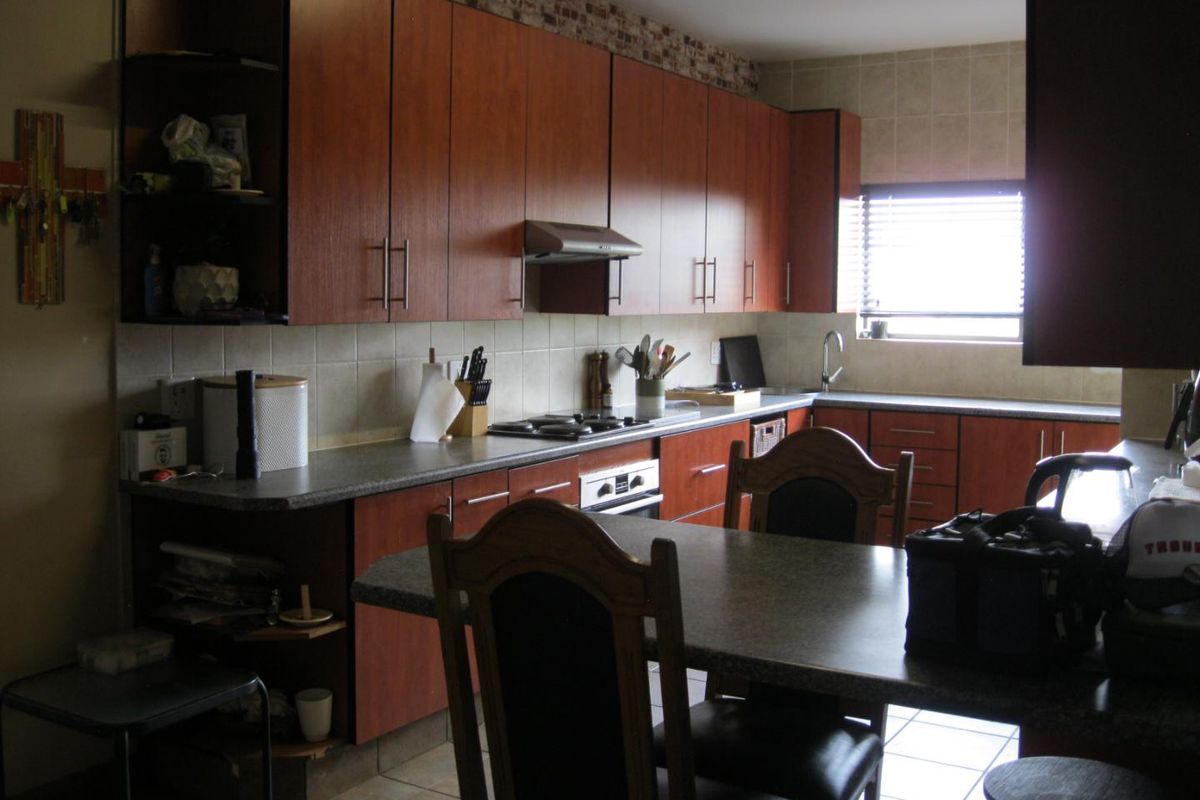 A functional kitchen featuring wood-finish cabinetry, tiled splashbacks, a built-in hob and oven, and an integrated breakfast nook area.