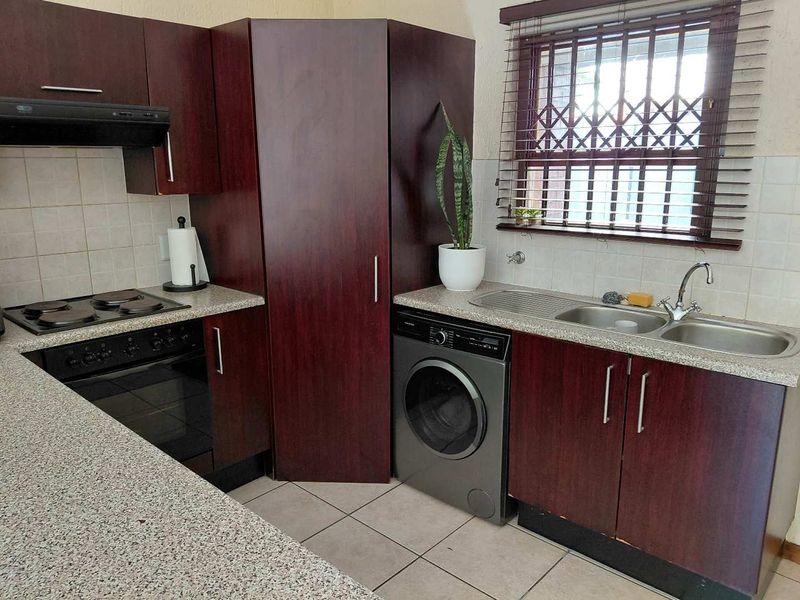 Functional kitchen featuring dark wood cabinetry, laminate countertops, integrated oven and hob, double sink, and security bars on the window.