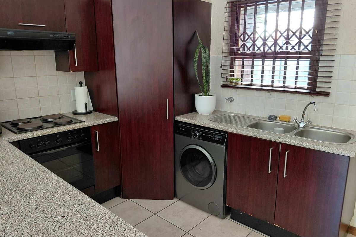 Functional kitchen featuring dark wood cabinetry, laminate countertops, integrated oven and hob, double sink, and security bars on the window.