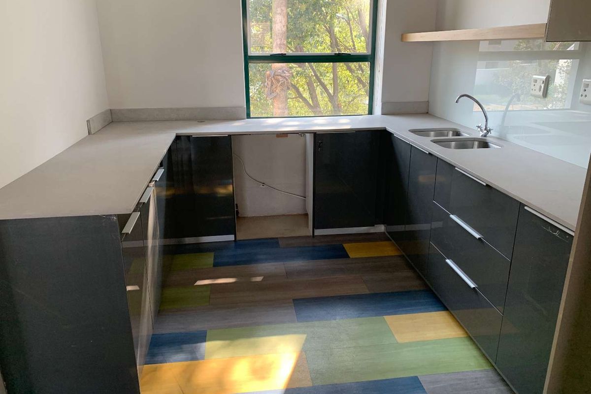 Modern office kitchenette featuring dark grey cabinetry, stone-look countertops, stainless steel sink, and vibrant multi-colored vinyl flooring.