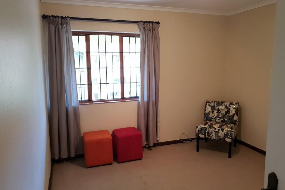 A neutrally painted bedroom featuring carpeted flooring and a window fitted with security bars and curtain tracks.