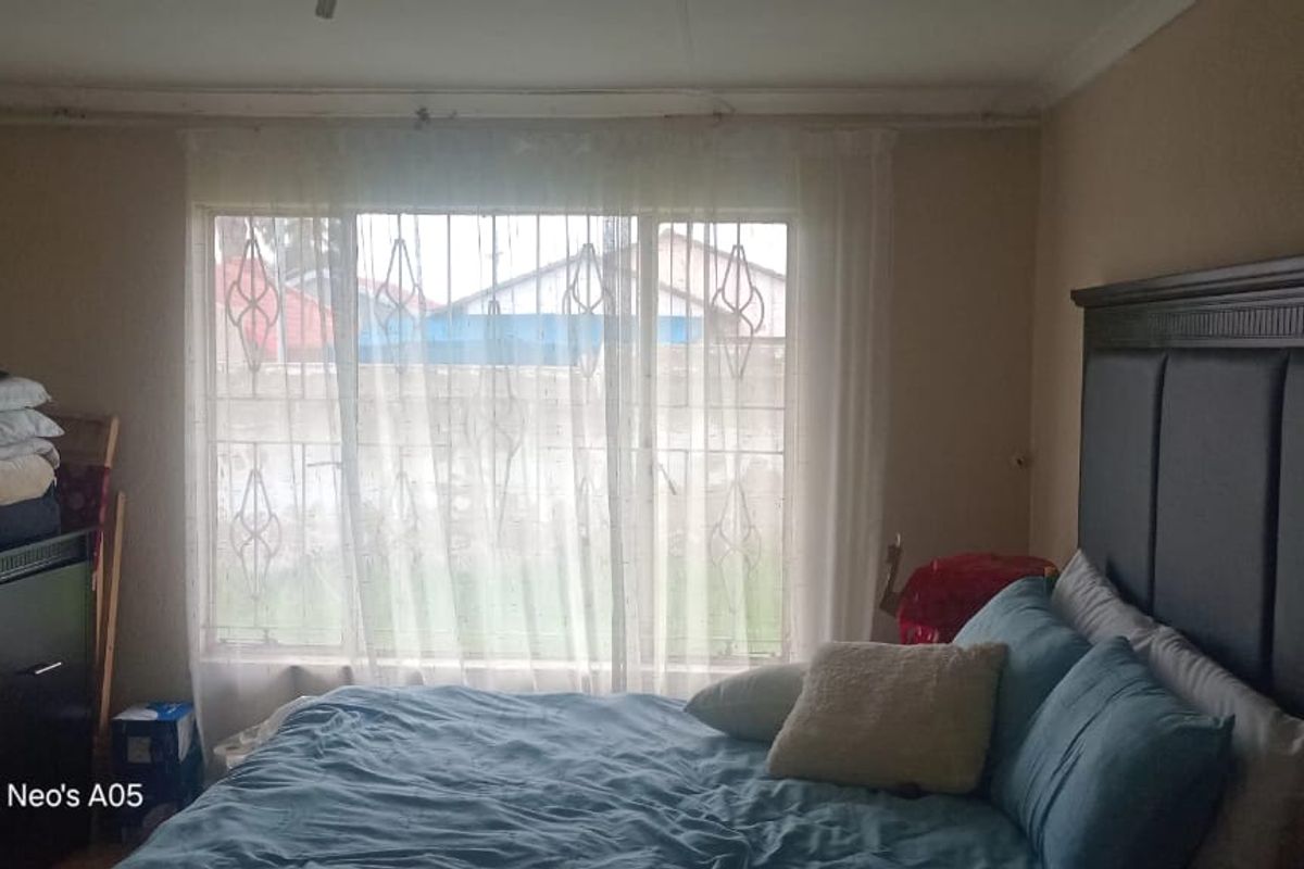 A bedroom featuring a large window with security bars, providing natural light and a view of the exterior property.