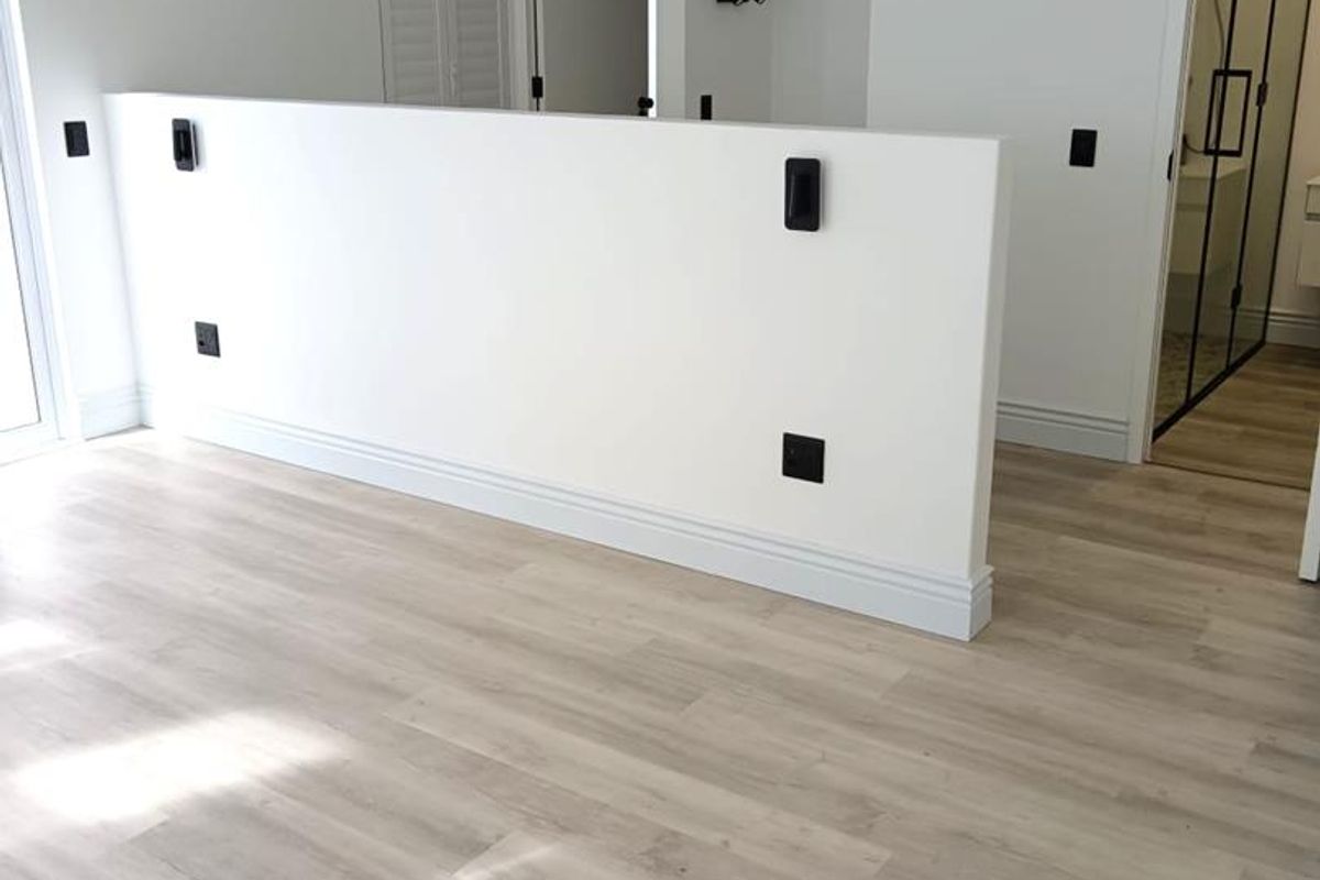 A bright, modern bedroom featuring light-toned laminate flooring, a central partition wall, and clean white finishes, offering a versatile and well-maintained living space.