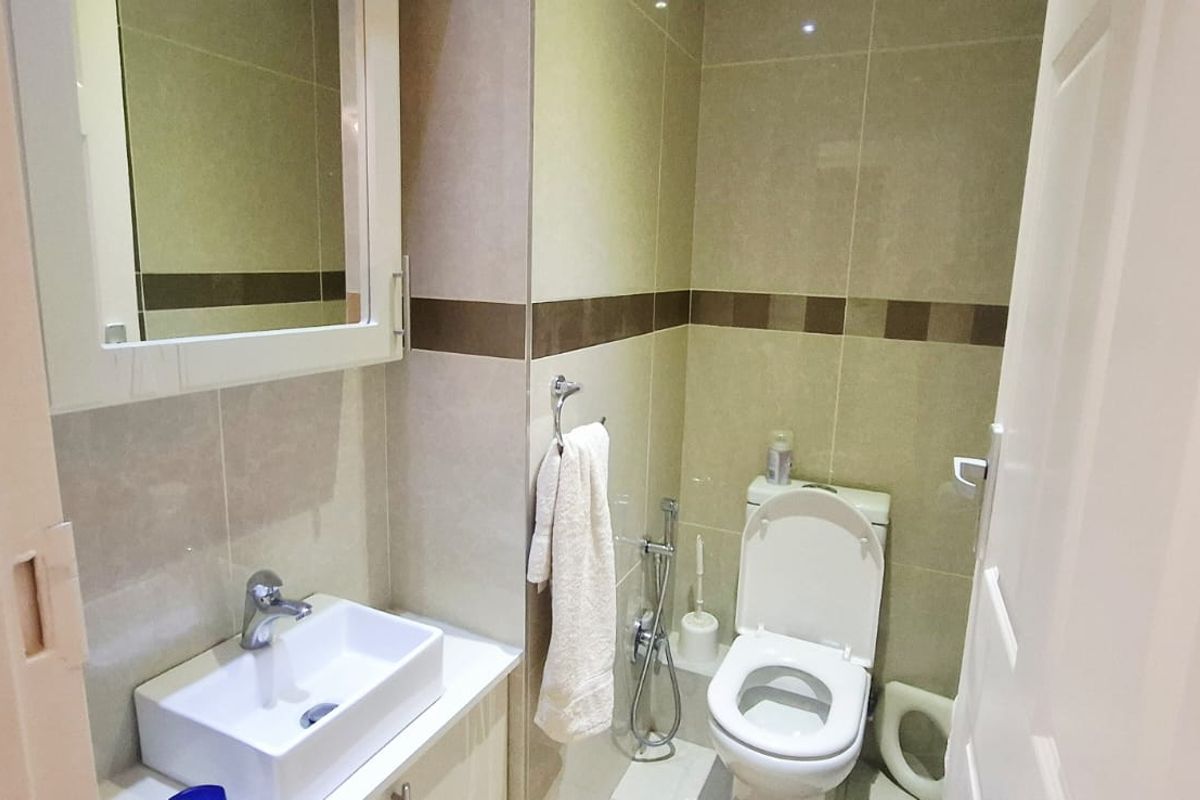 A compact bathroom featuring a modern vessel sink, vanity cabinet, wall-mounted mirror, and a standard toilet with a bidet spray attachment.