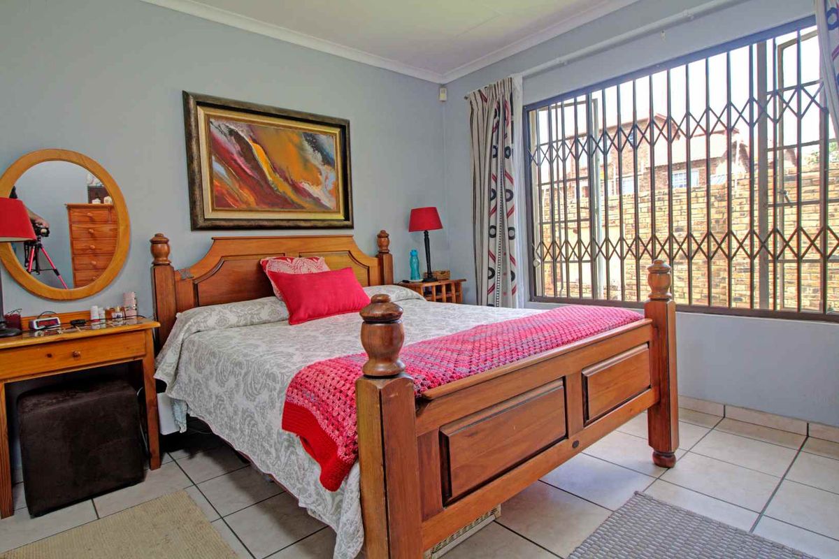 A bedroom featuring tiled flooring and a large window fitted with security bars, providing natural light and ventilation.
