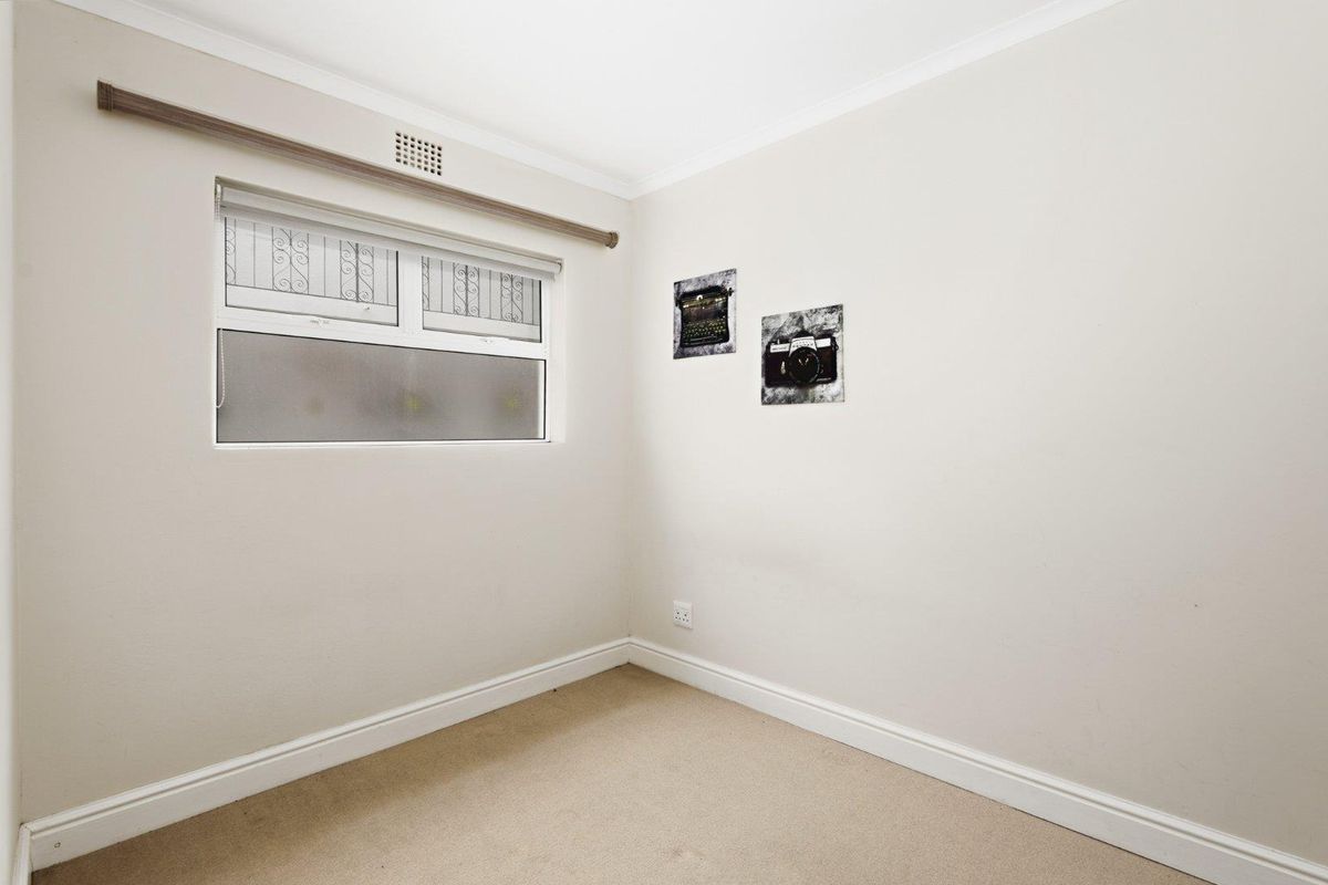 A clean, empty bedroom featuring neutral walls, carpeted flooring, and a window fitted with security bars.