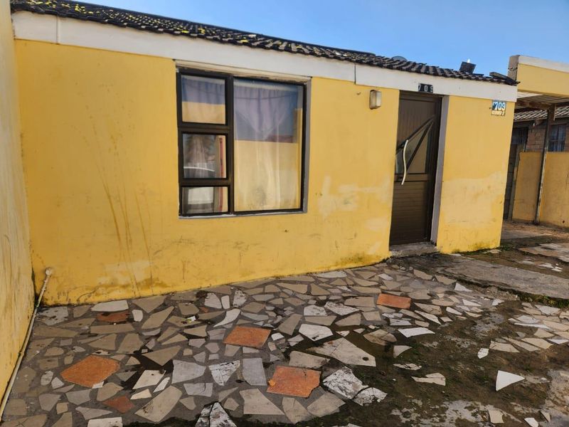 Front exterior view of a single-story house featuring a yellow facade, tiled patio area, and a single entrance door.