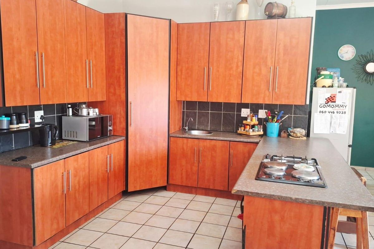 A functional kitchen featuring wood-look laminate cabinetry, dark tiled splashbacks, a built-in gas hob, and tiled flooring.