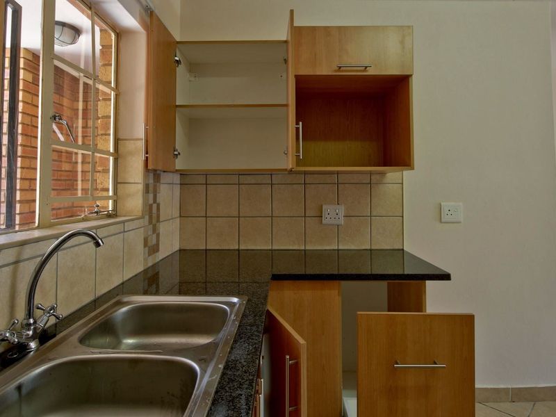 A compact kitchen featuring granite countertops, a double stainless steel sink, and laminate cabinetry with some visible maintenance required.