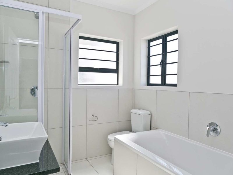 A clean, modern bathroom featuring a separate shower enclosure, bathtub, vessel sink with granite vanity, and neutral wall and floor tiling.