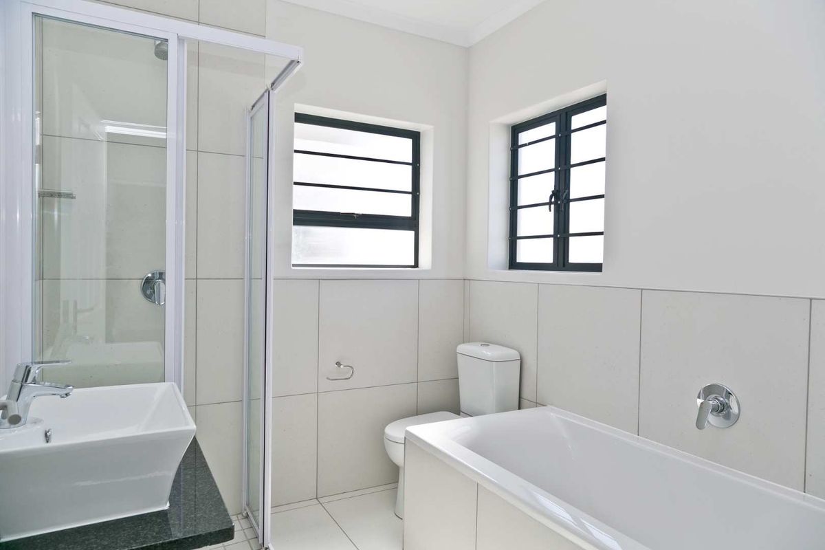 A clean, modern bathroom featuring a separate shower enclosure, bathtub, vessel sink with granite vanity, and neutral wall and floor tiling.