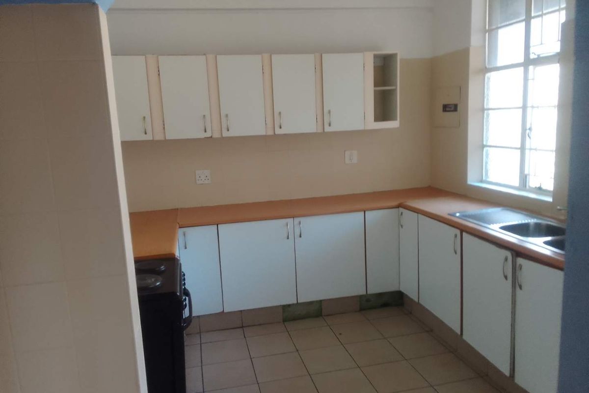 A functional kitchen featuring white built-in cabinetry, laminate countertops, a stainless steel sink, and tiled flooring, offering a blank canvas for renovation.