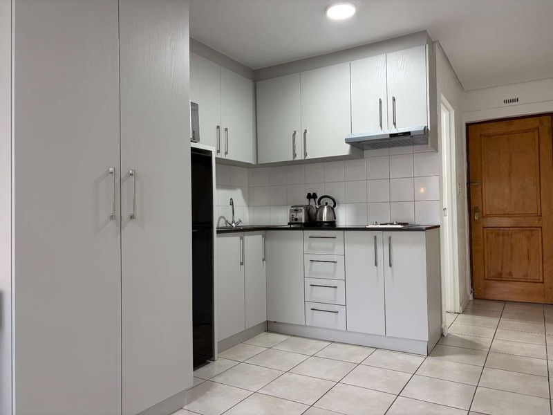 A compact, well-maintained kitchen featuring light-toned cabinetry, tiled flooring, a tiled backsplash, and integrated extractor fan.