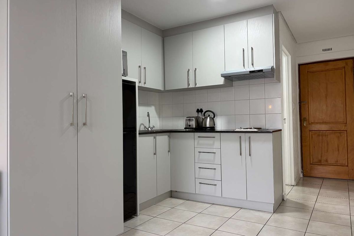 A compact, well-maintained kitchen featuring light-toned cabinetry, tiled flooring, a tiled backsplash, and integrated extractor fan.