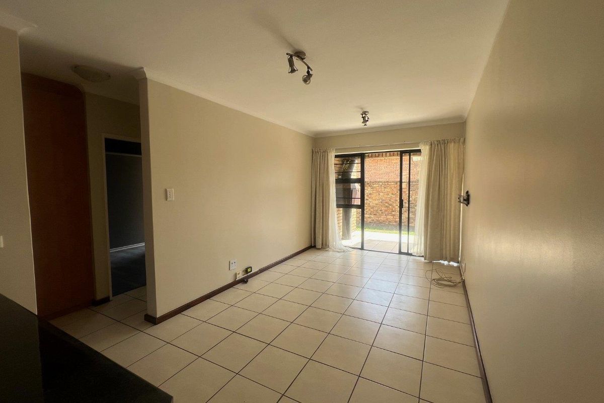 A bright, empty living room featuring neutral tiled flooring and a sliding glass door providing access to the outdoor area.