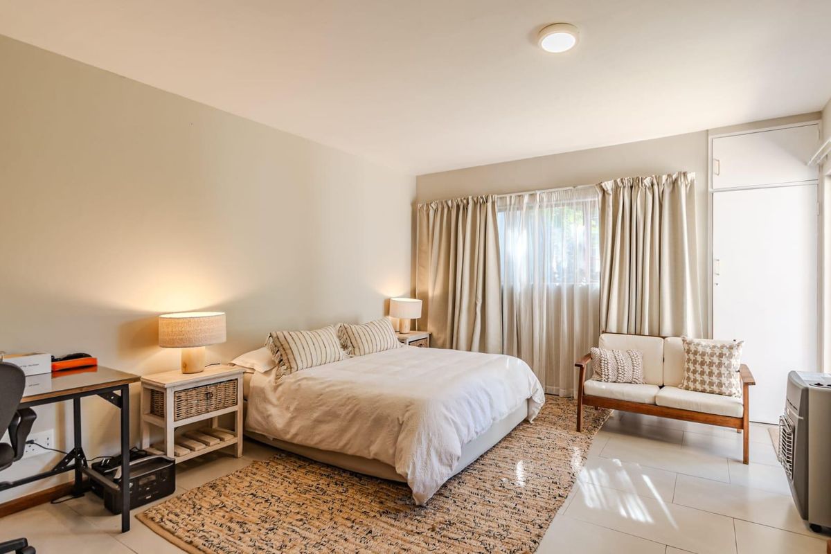 A well-lit bedroom featuring neutral wall tones, tiled flooring, and a built-in cupboard, offering a comfortable and functional living space.