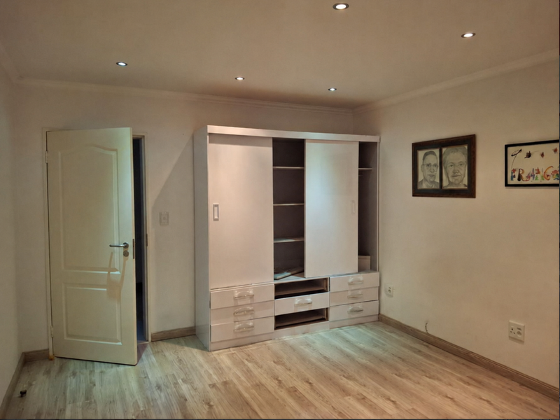 A bright bedroom featuring light-toned laminate flooring, recessed ceiling downlights, and a functional built-in wardrobe with sliding doors.