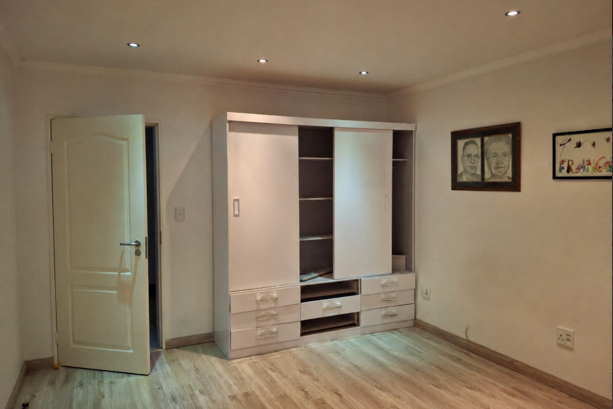 A bright bedroom featuring light-toned laminate flooring, recessed ceiling downlights, and a functional built-in wardrobe with sliding doors.