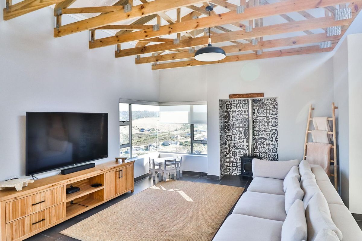 Spacious living room featuring exposed timber roof trusses, a feature wall with patterned tiling, a built-in fireplace, and large windows with scenic views.