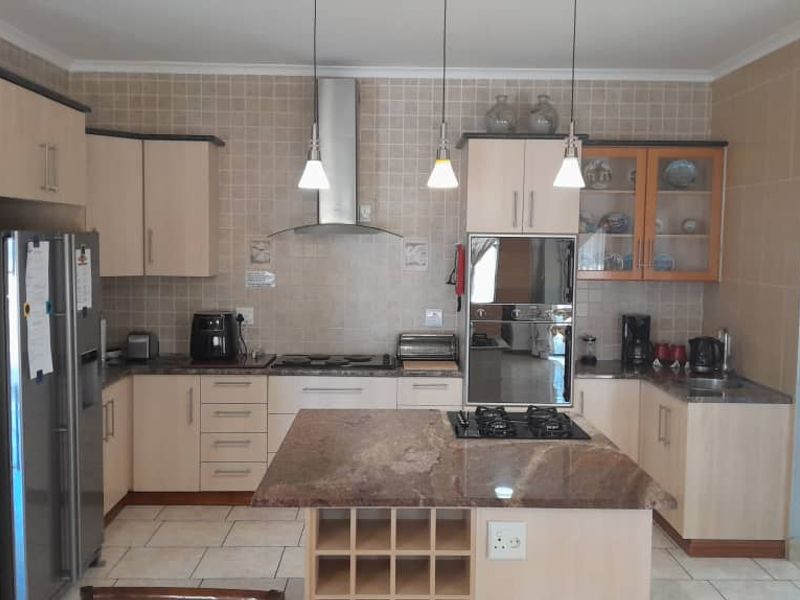 A well-appointed kitchen featuring granite countertops, a central island with a gas hob, built-in oven, extractor fan, and ample cabinetry with a tiled backsplash.