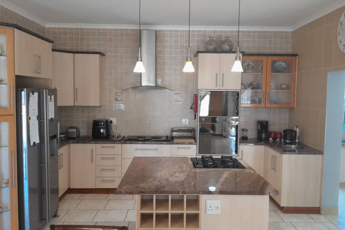 A well-appointed kitchen featuring granite countertops, a central island with a gas hob, built-in oven, extractor fan, and ample cabinetry with a tiled backsplash.