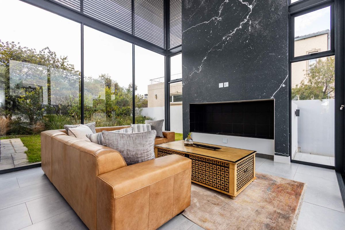 Modern living room featuring floor-to-ceiling glass walls, a striking black marble-clad fireplace, and large format floor tiles with seamless garden views.