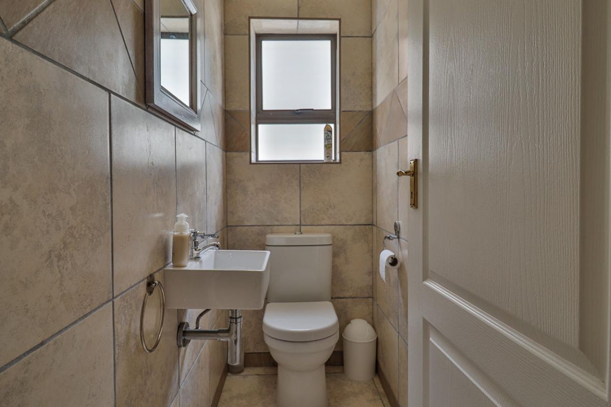 A compact guest bathroom featuring floor-to-ceiling tiled walls, a wall-mounted basin, and a standard toilet.