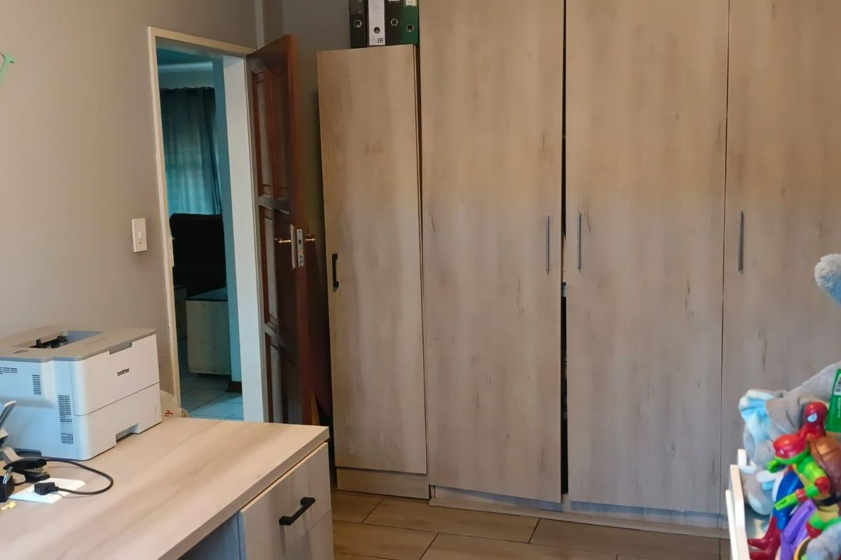 A bedroom featuring built-in light wood-grain cabinetry and tiled flooring, with an adjacent doorway leading to another living space.