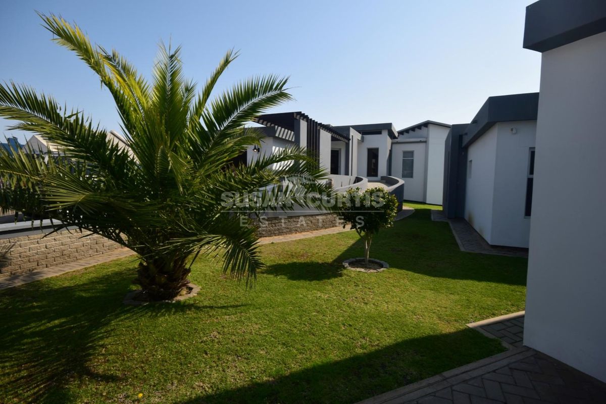 A well-maintained rear garden area featuring a paved walkway, manicured lawn, and established landscaping surrounding the modern building exterior.