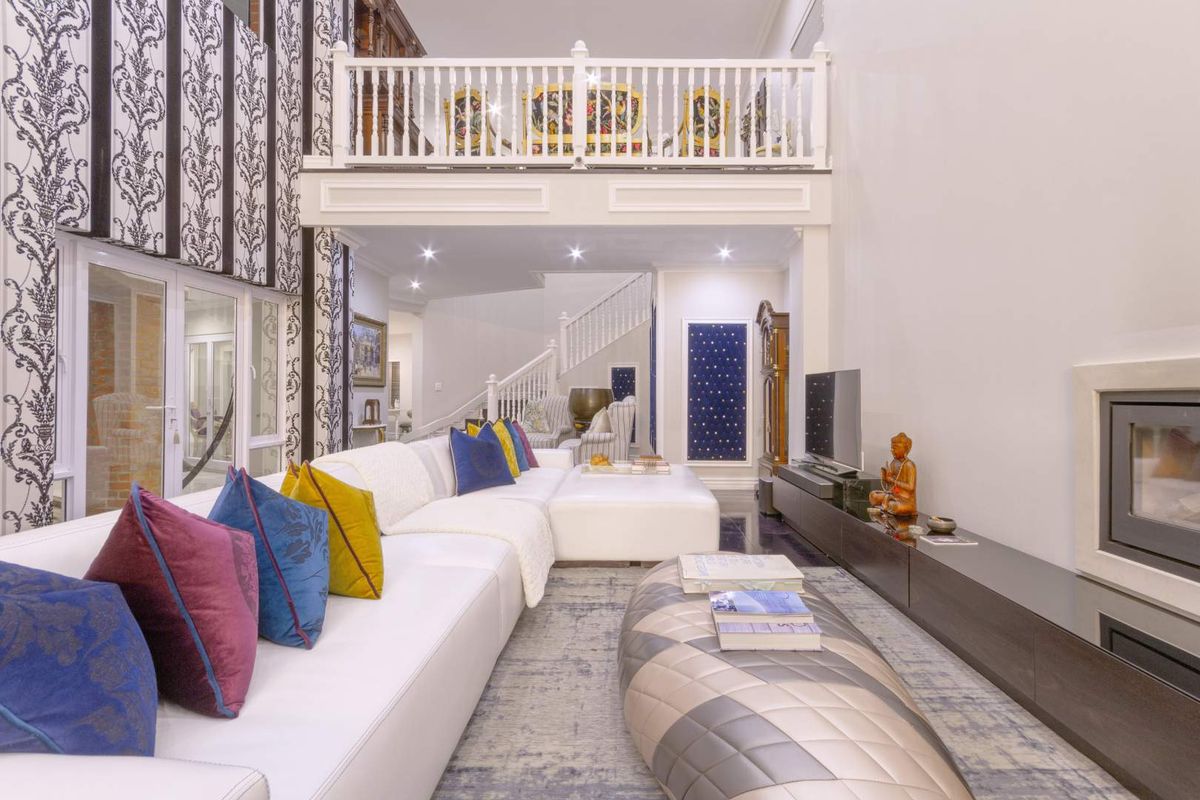 Spacious double-volume living room featuring a built-in fireplace, elegant mezzanine balcony, and a staircase leading to the upper level.
