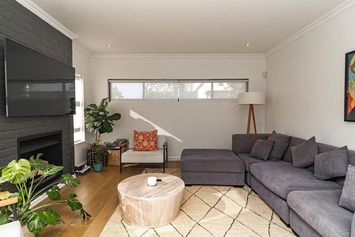 A well-maintained living room featuring a dark painted brick fireplace, timber flooring, and a horizontal clerestory window providing natural light.
