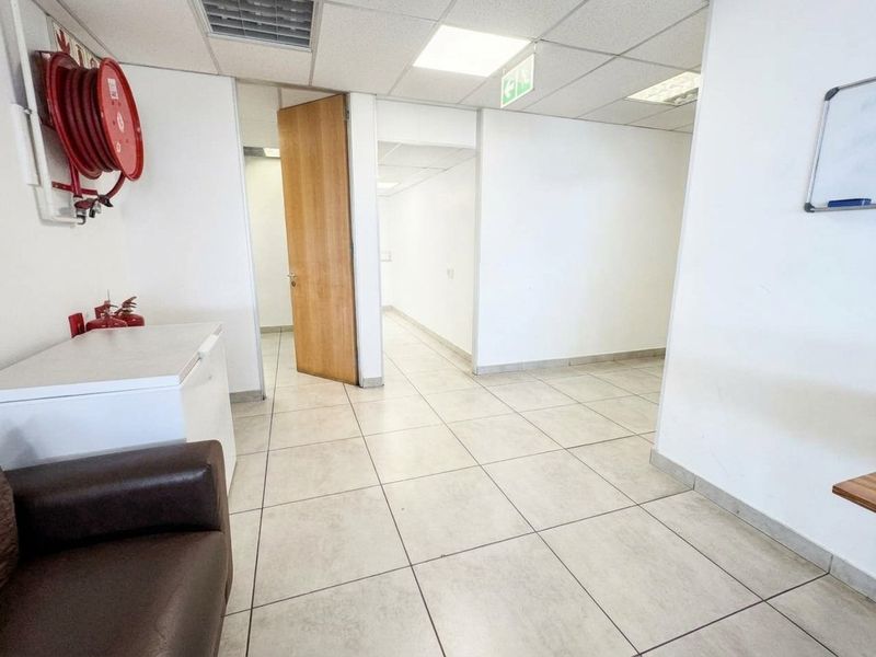A functional office space featuring tiled flooring, a suspended ceiling with recessed lighting, and a wall-mounted fire hose reel.