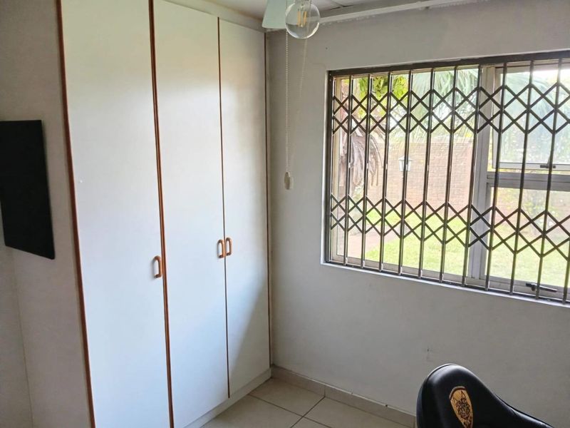 A bedroom featuring built-in cupboards, tiled flooring, and a window fitted with a security gate.