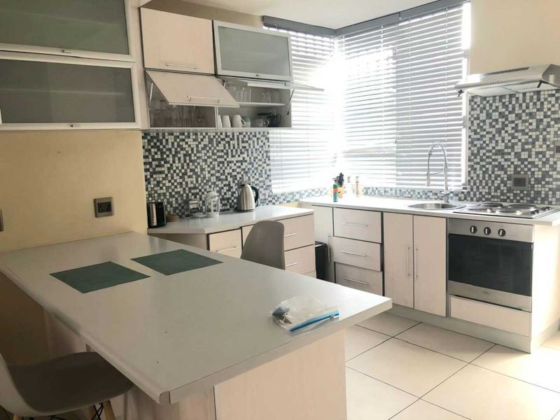 A functional kitchen featuring built-in cabinetry, a mosaic tile backsplash, integrated stainless steel appliances, and a convenient breakfast bar area.