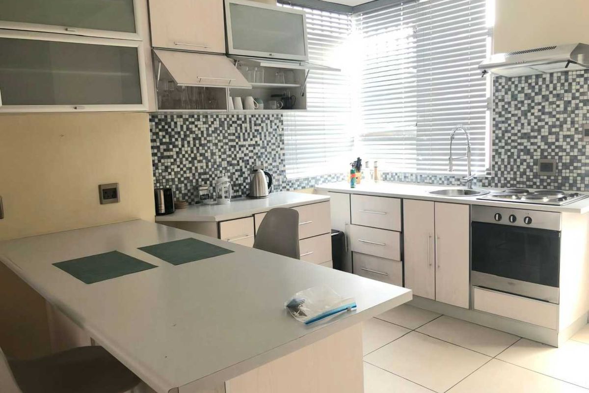 A functional kitchen featuring built-in cabinetry, a mosaic tile backsplash, integrated stainless steel appliances, and a convenient breakfast bar area.