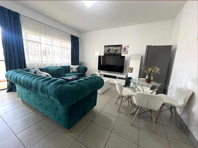 A bright living area featuring neutral tiled flooring and a large window with security bars, providing ample natural light to the space.