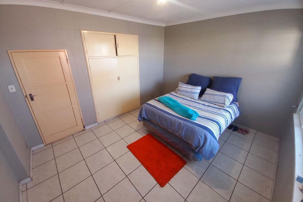 A functional bedroom featuring tiled flooring, built-in storage cupboards, and a neutral wall finish.