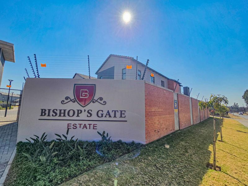 The entrance to Bishop's Gate Estate featuring a prominent brick and plastered boundary wall with integrated electric security fencing and paved access.