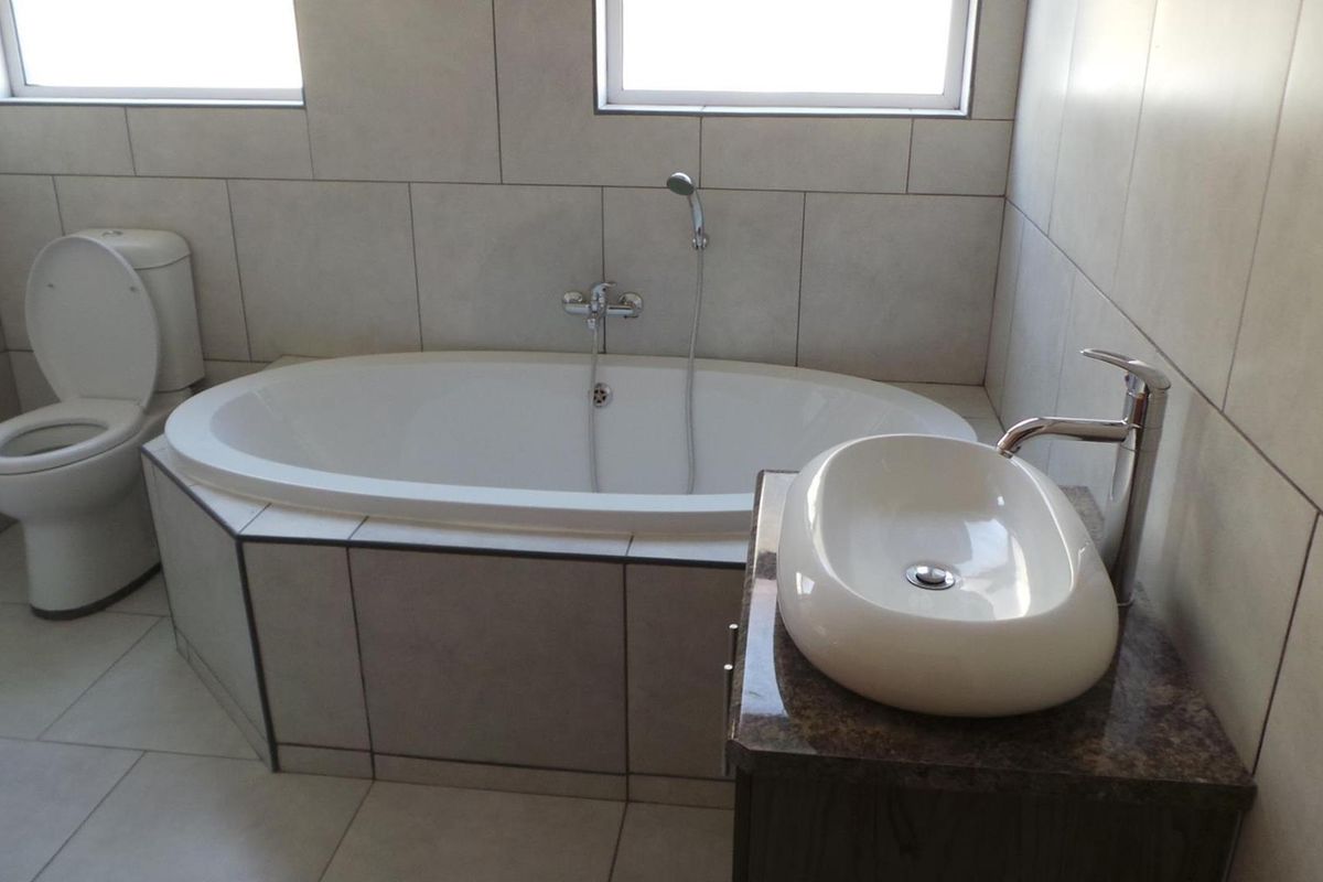 A modern bathroom featuring a built-in oval bathtub, a ceramic vessel sink on a stone vanity, and neutral wall tiling.
