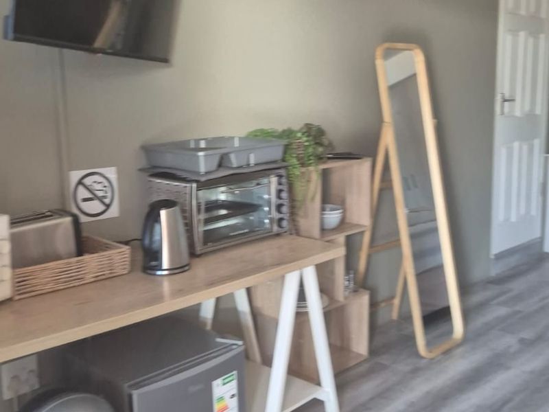 A living area featuring light-toned laminate flooring and neutral wall finishes, providing a functional space with access to an adjoining room.