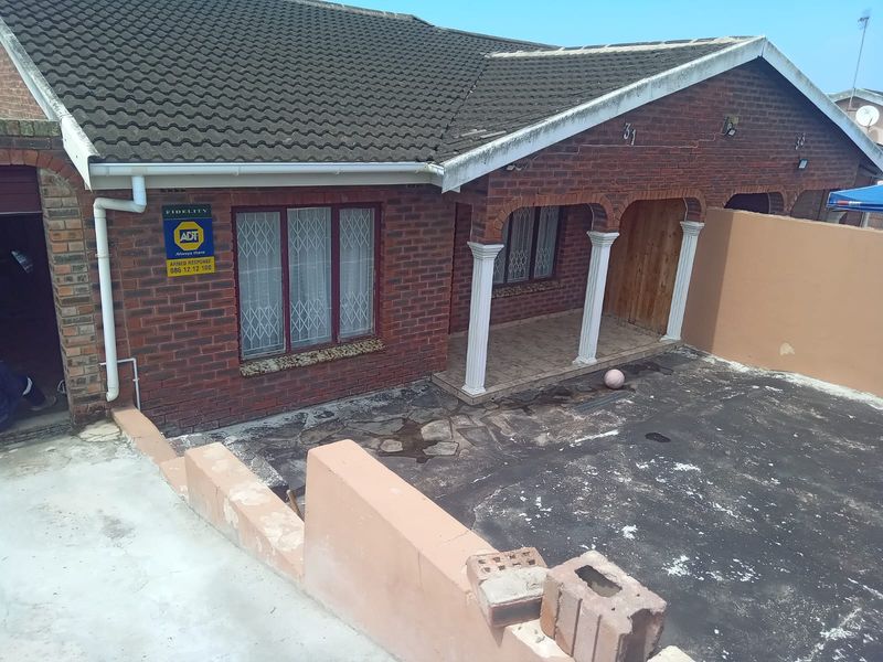 Front elevation of a brick house featuring a covered porch with decorative columns, security bars on windows, and a paved driveway area.