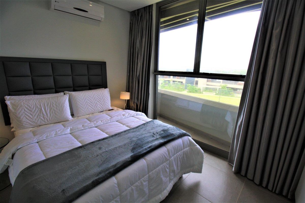 Modern bedroom featuring tiled flooring, a wall-mounted air conditioning unit, and large sliding glass doors providing access to a private balcony.