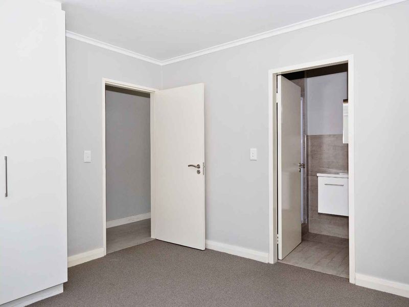 A clean, neutral bedroom featuring built-in wardrobes, carpeted flooring, and direct access to an en-suite bathroom.