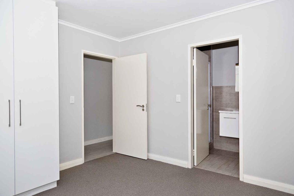 A clean, neutral bedroom featuring built-in wardrobes, carpeted flooring, and direct access to an en-suite bathroom.