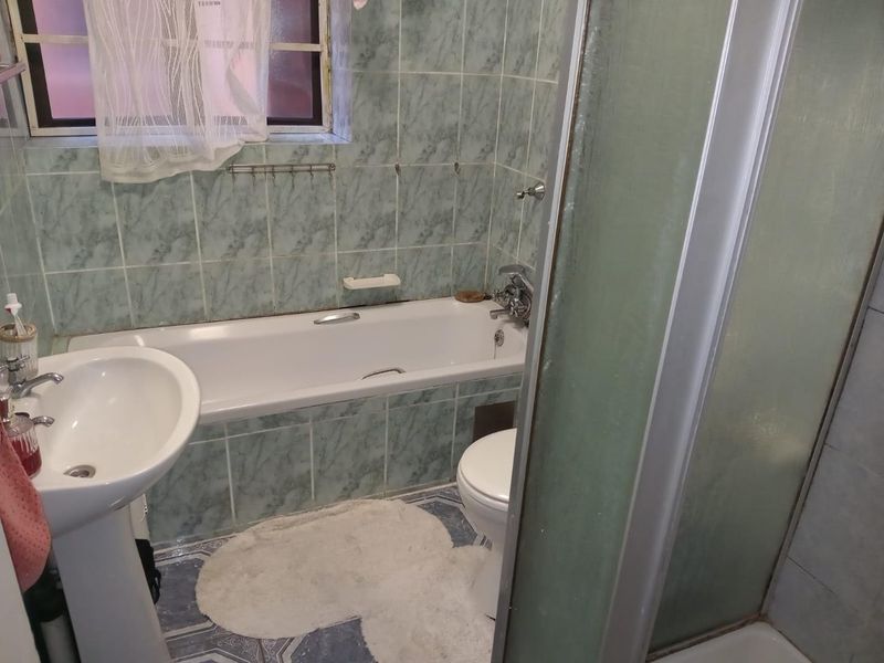 A functional bathroom featuring a pedestal basin, bathtub, and separate shower enclosure with dated wall and floor tiling.