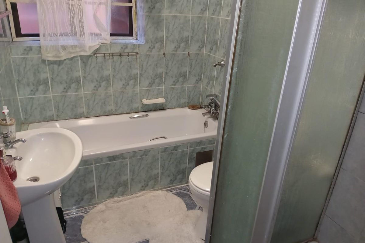 A functional bathroom featuring a pedestal basin, bathtub, and separate shower enclosure with dated wall and floor tiling.